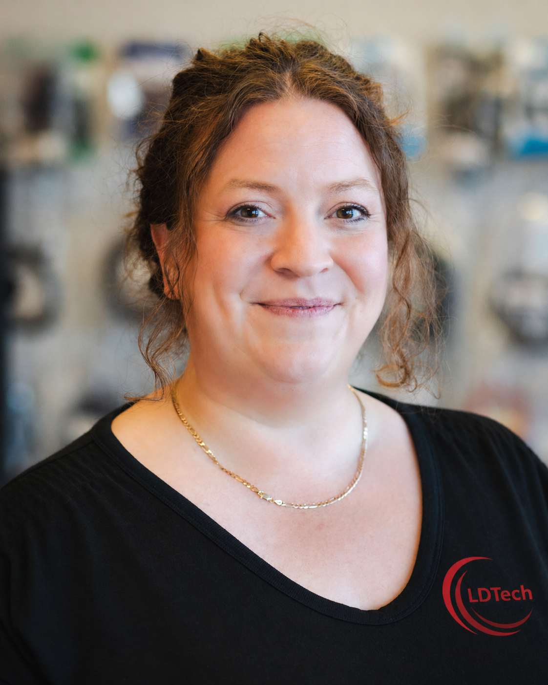 Portrait of a smiling woman with brown hair in a black LDTech shirt, indoors.